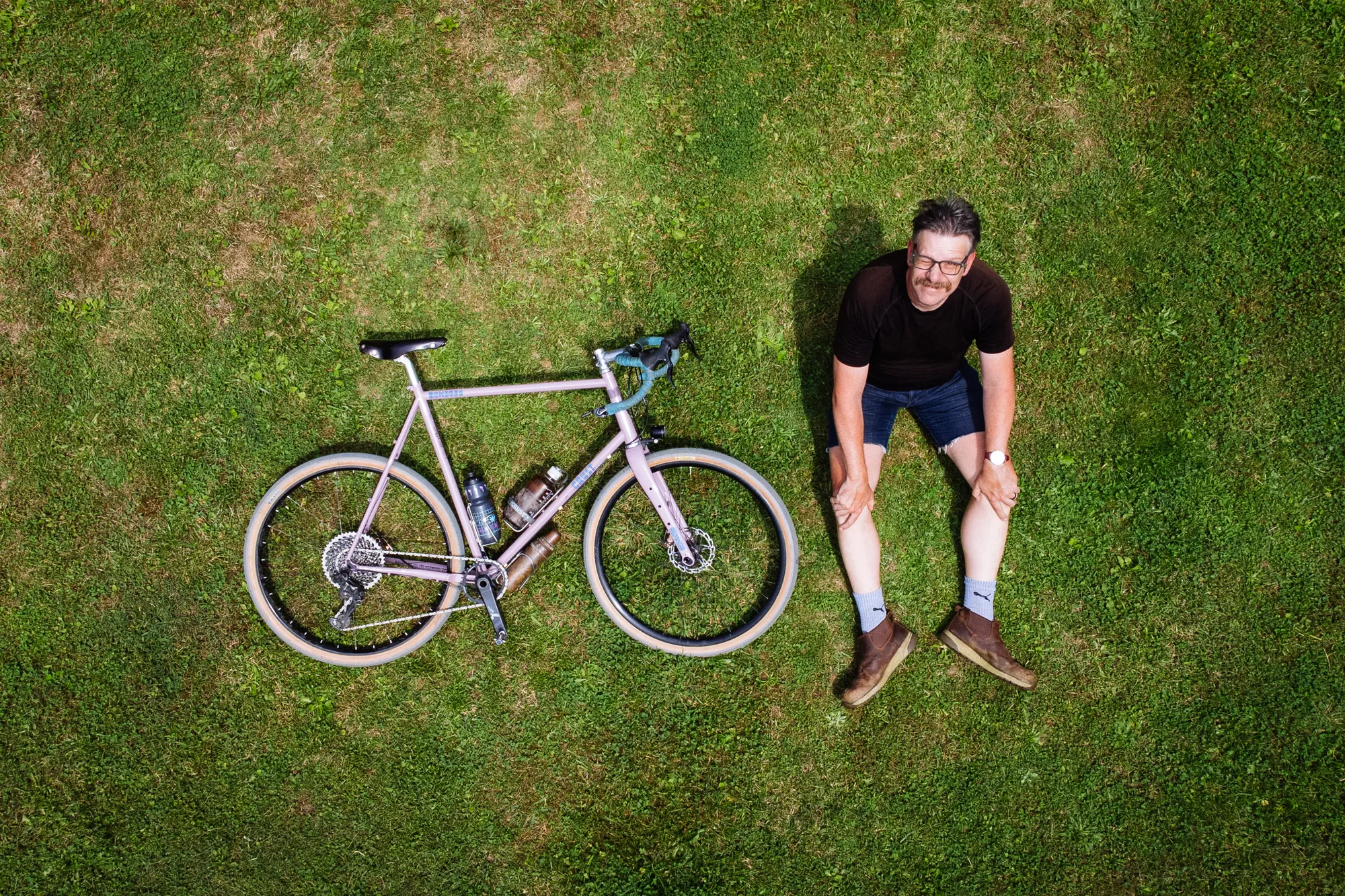 John McCaig lying on a lawn next to his bicycle, photographed from directly above